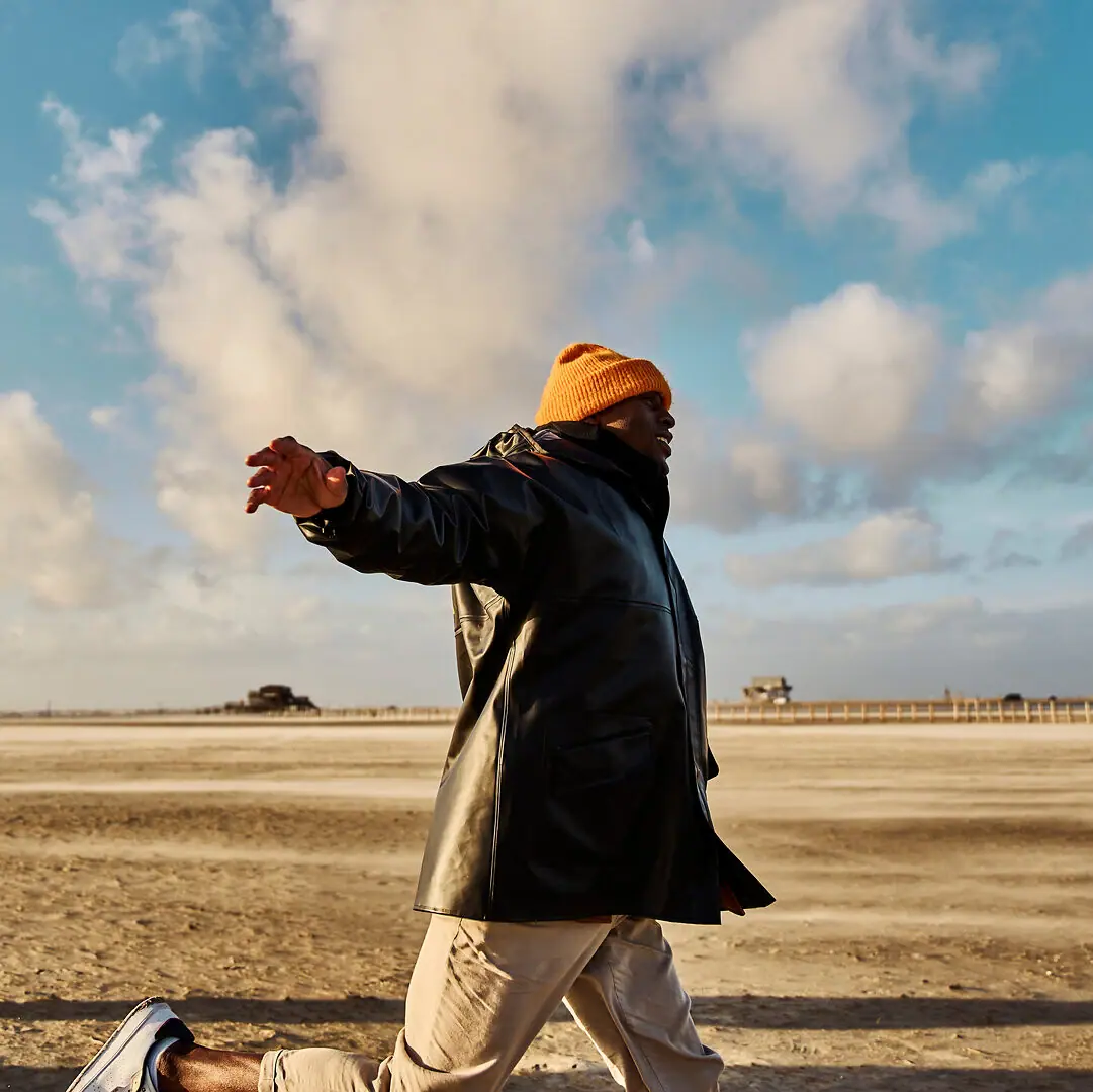 Walk on the beach A man in a black coat and orange hat stands on the sandy beach.