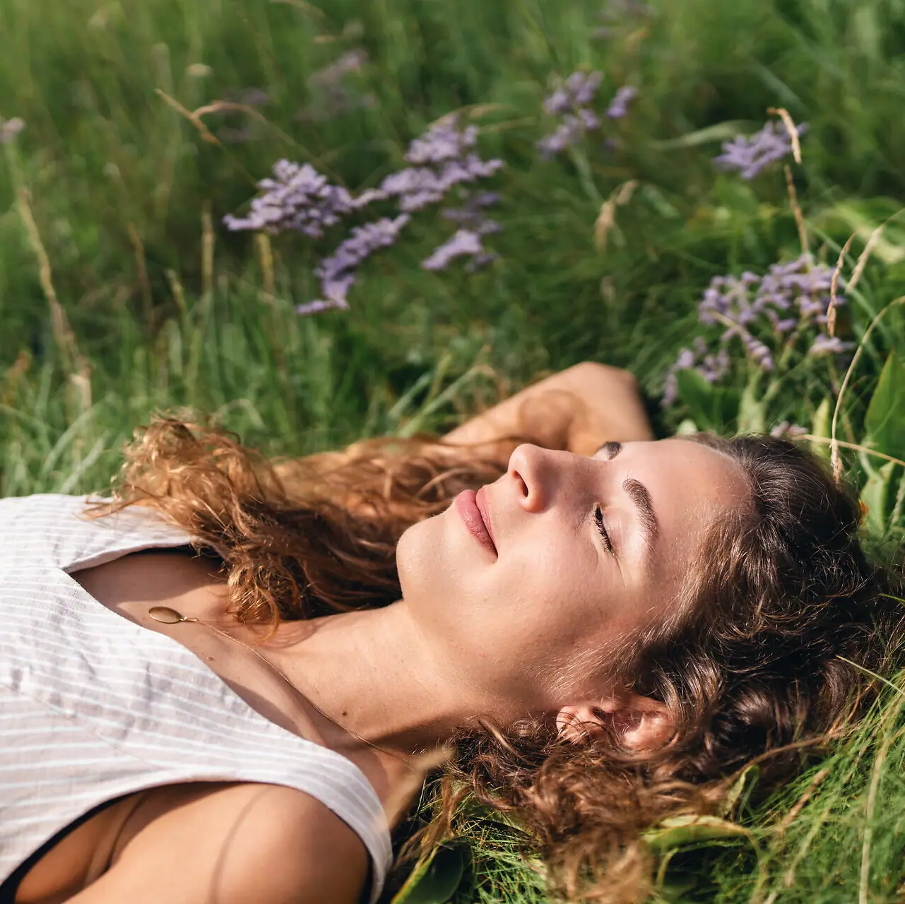 A woman is lying in the grass in the salt marshes of St Peter-Ording, her eyes closed.
